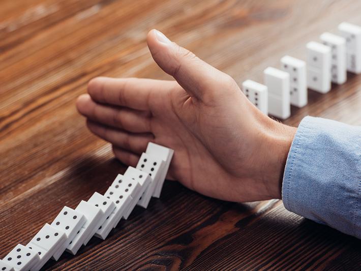 Hand stopping a line of dominoes falling