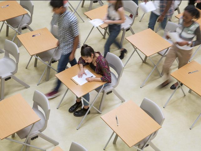 A student sits an exam hall as her peers leave around her