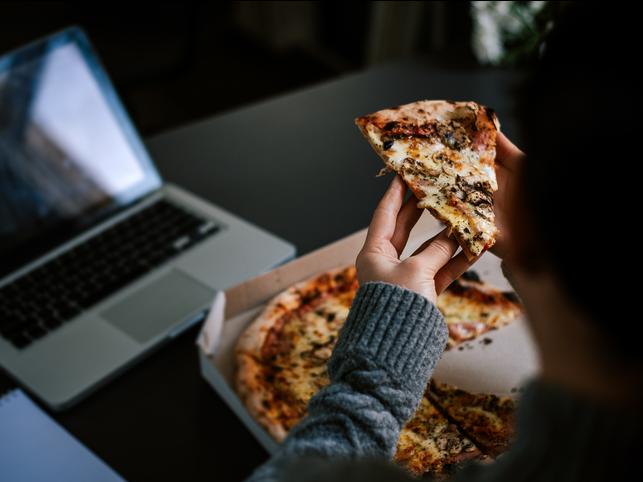 A student eats pizza in front of a laptop