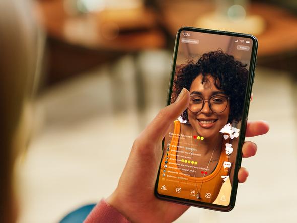 A hand holds a phone, on which an influencer is live streaming