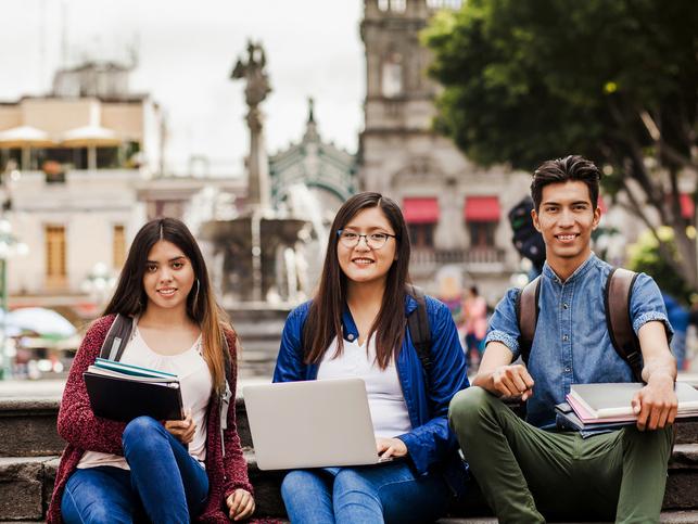 Three international students sitting in front of a landmark