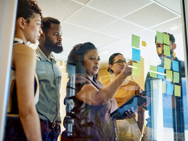 Staff and students strategising with Post-It notes on a transparnt screen