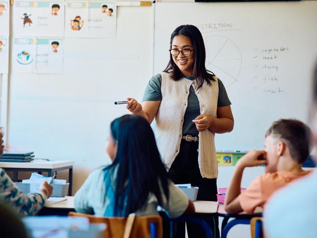 A schoolteacher standing in front of a whiteboard interacting with pupils