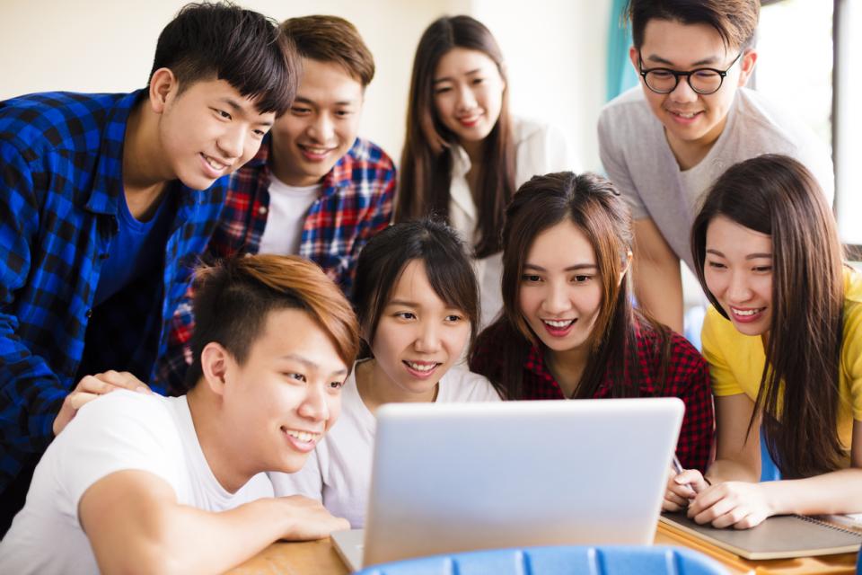 East Asian students crowding around a laptop in class