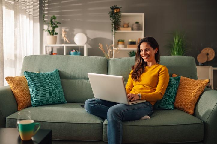 A woman sits on a sofa with a laptop