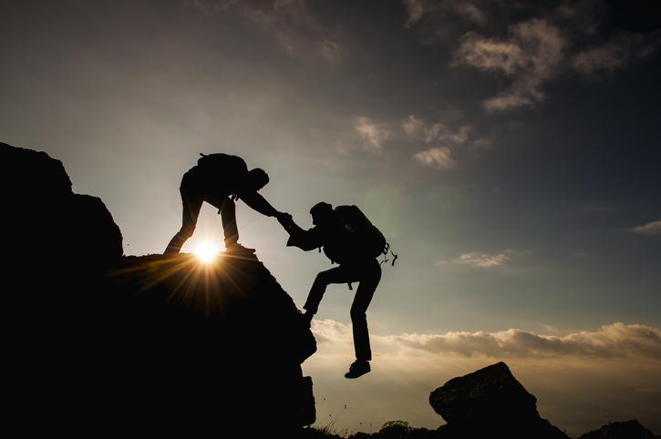 One mountain climber helps another over a ridge