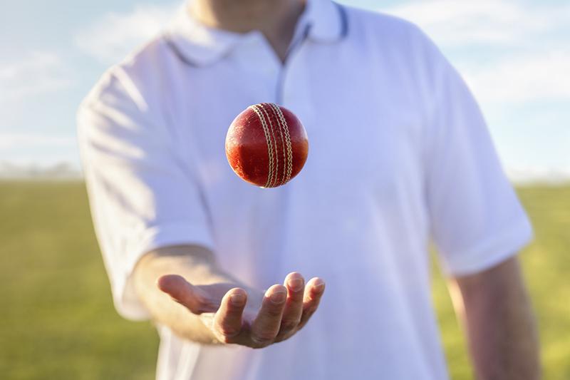 Cricket player tossing ball in hand on pitch