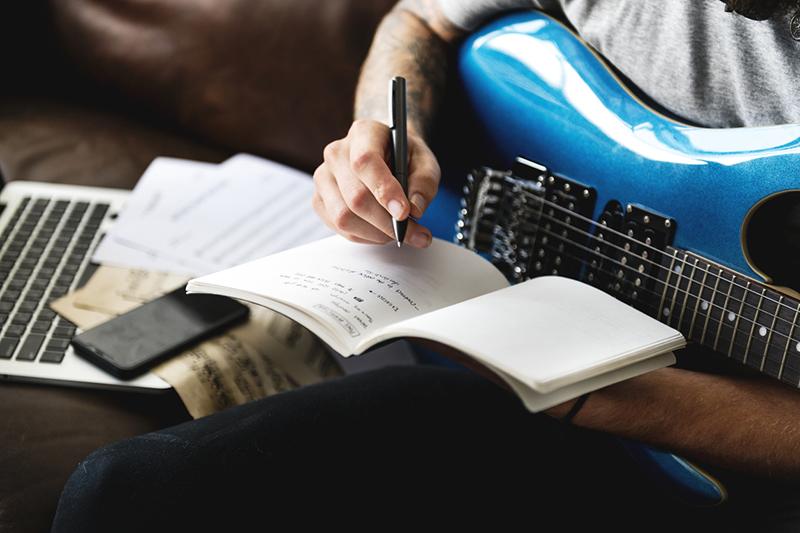 Detail of man writing music on an electric guitar