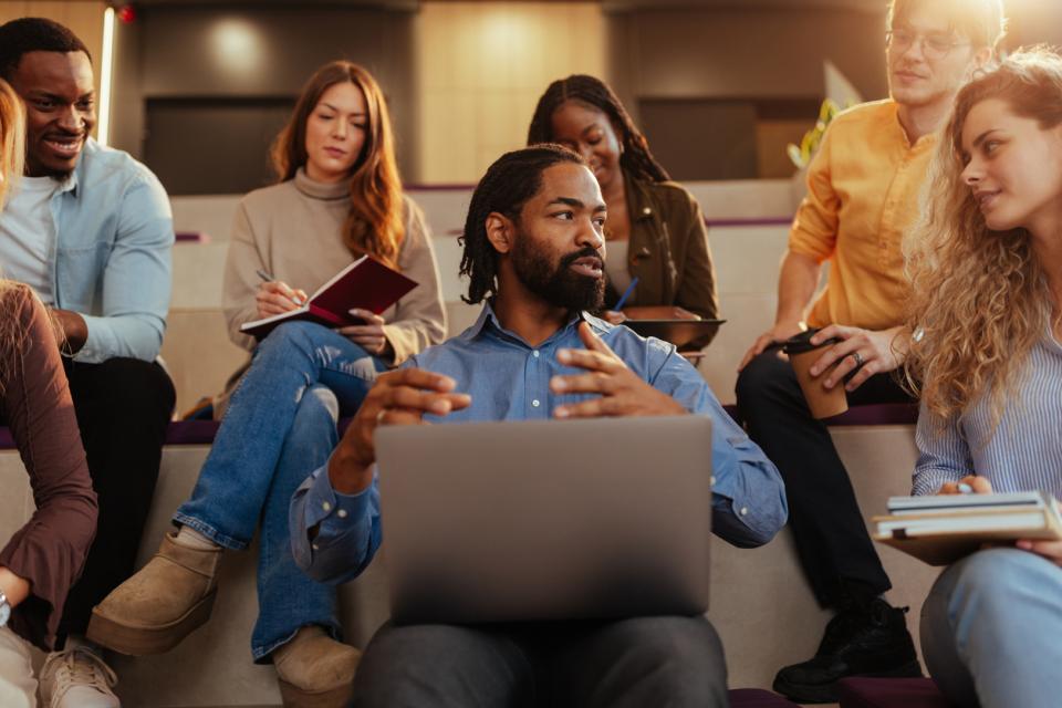 A university lecturer explaining a concept while sitting amongst students 