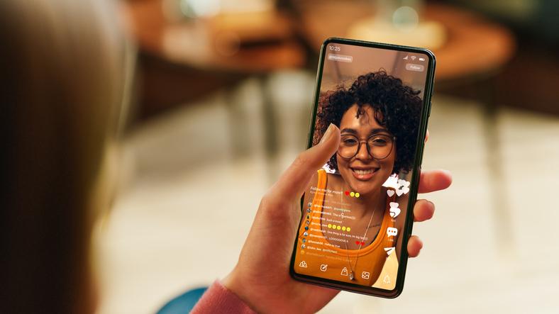 A hand holds a phone, on which an influencer is live streaming