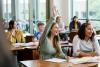 Students in class watching a teacher, among them one raises her hand to answer a question