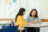 A student and teacher sitting at a desk discussing an assignment
